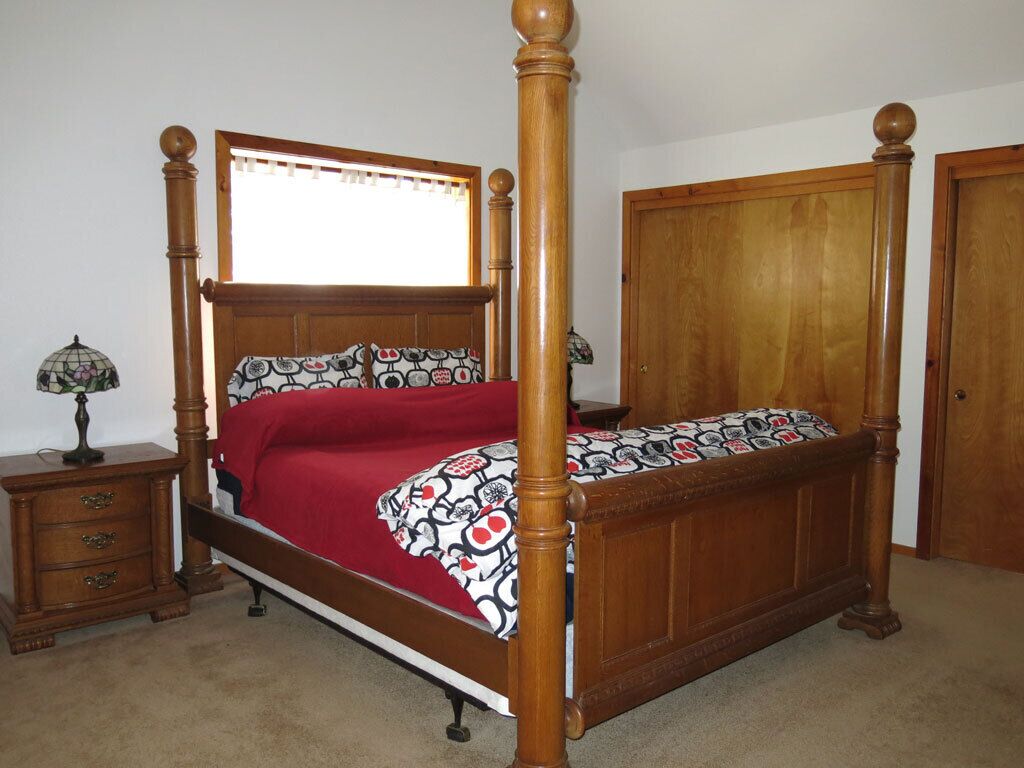 Ein Bett mit Baldachin, dessen Gestell aus Holz besteht und das mit einer roten Bettdecke bezogen ist.