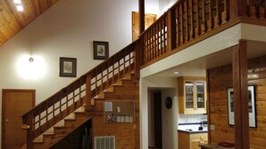 Un escalier en bois menant à une chambre aménagée en mezzanine, un salon avec un canapé et un coin cuisine.