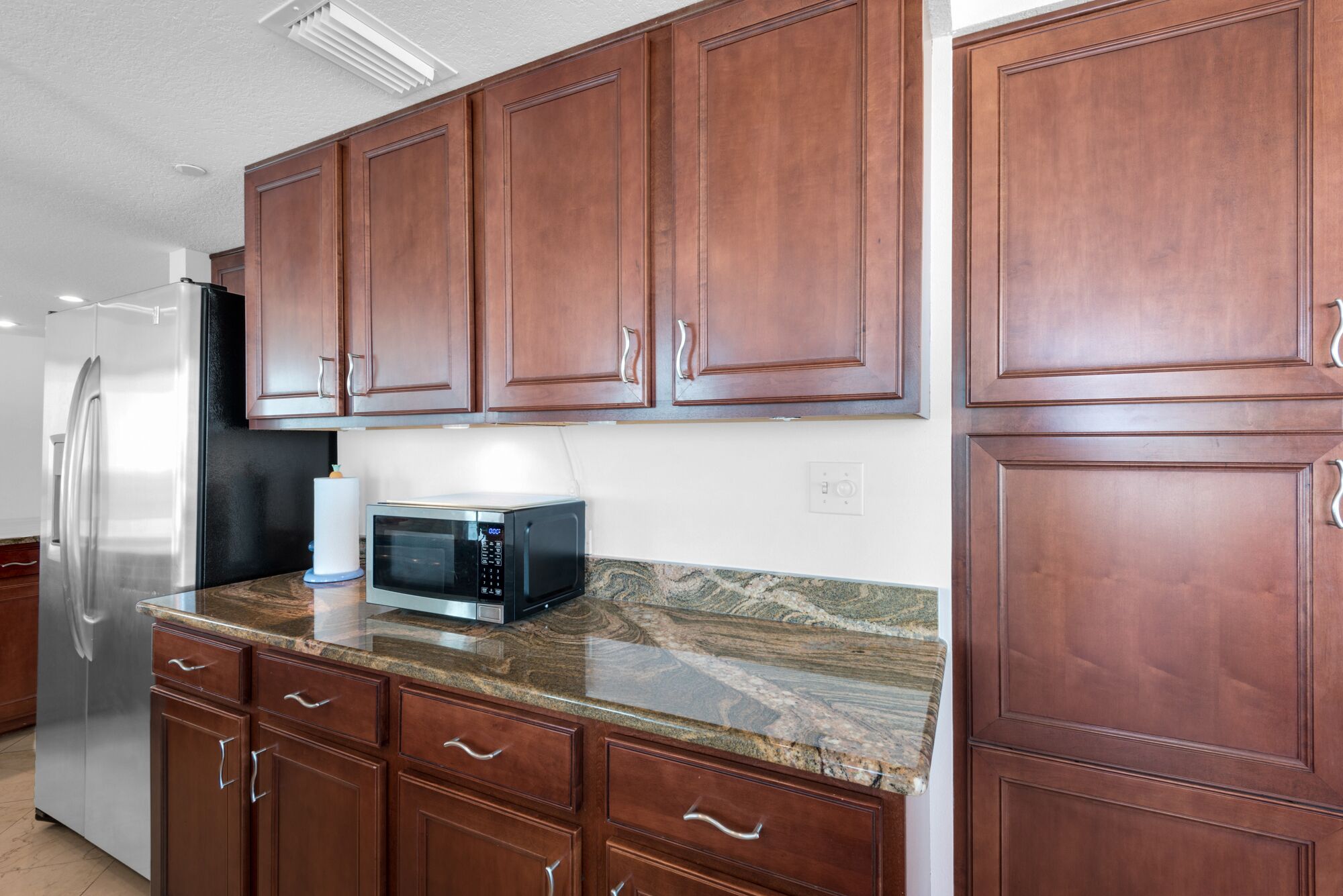 A kitchen with wooden cabinets, a stainless steel refrigerator, a microwave, and granite countertops.