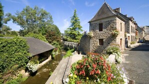 Un edificio de piedra con un techo empinado, un pequeño jardín con flores y un canal.