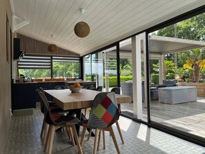 Eine moderne Küche mit einem Holztisch und Stühlen, einer Obstschale und Blick ins Freie durch große Glastüren.