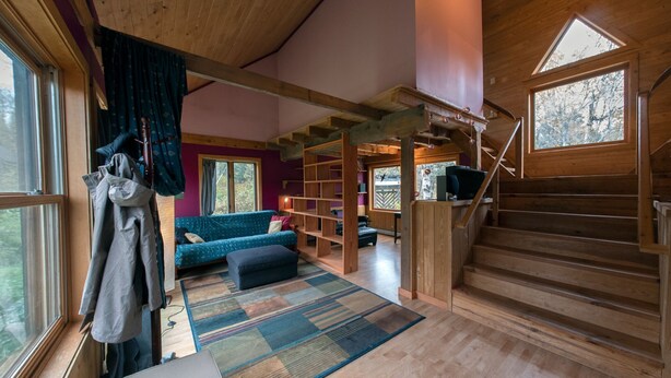 Ein geräumiges Zimmer mit einer Holztreppe, einem blauen Sofa, einem Bücherregal und einem großen Fenster.