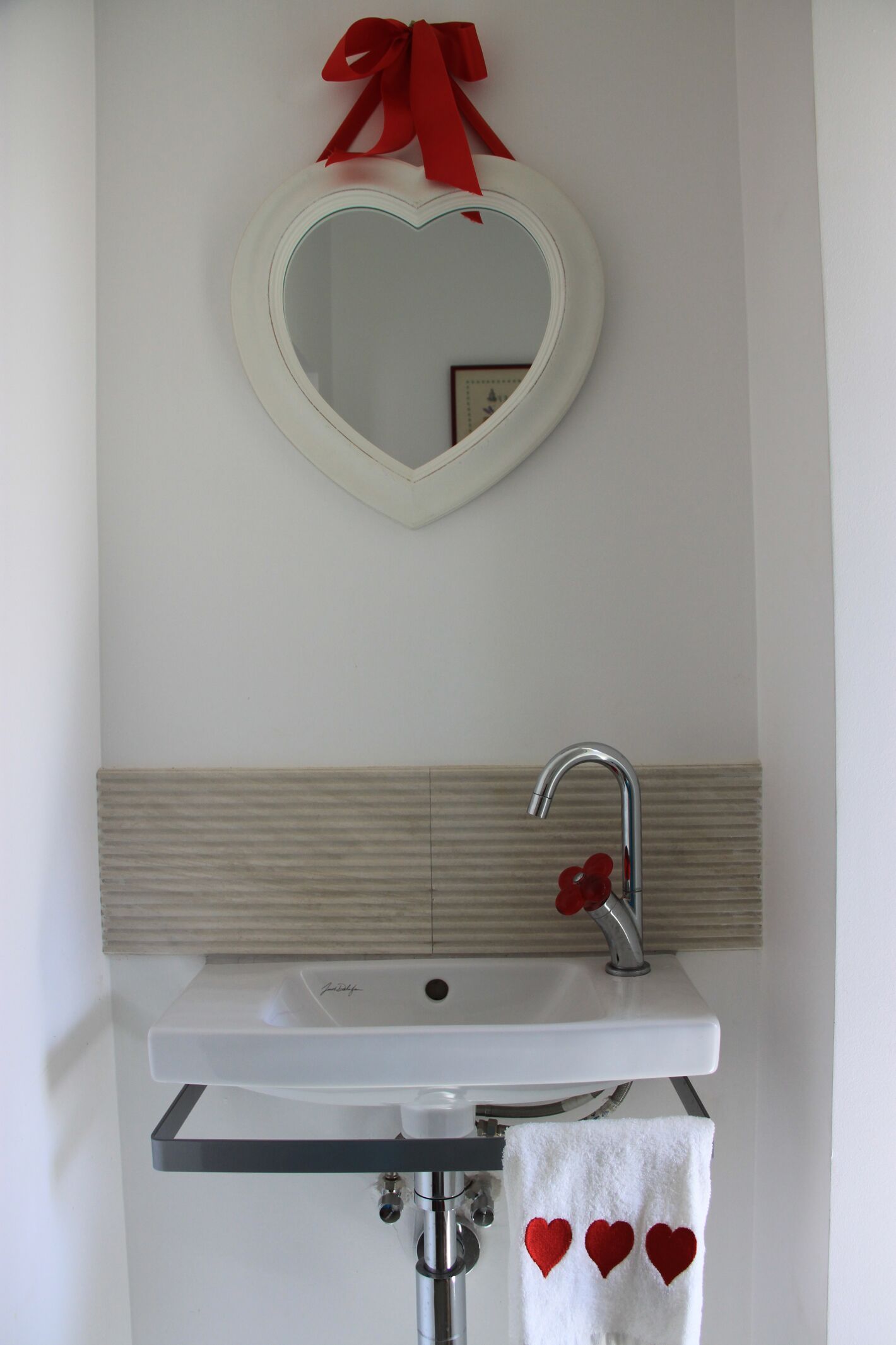 A bathroom with a heart-shaped mirror, a white sink, and a towel with red hearts.