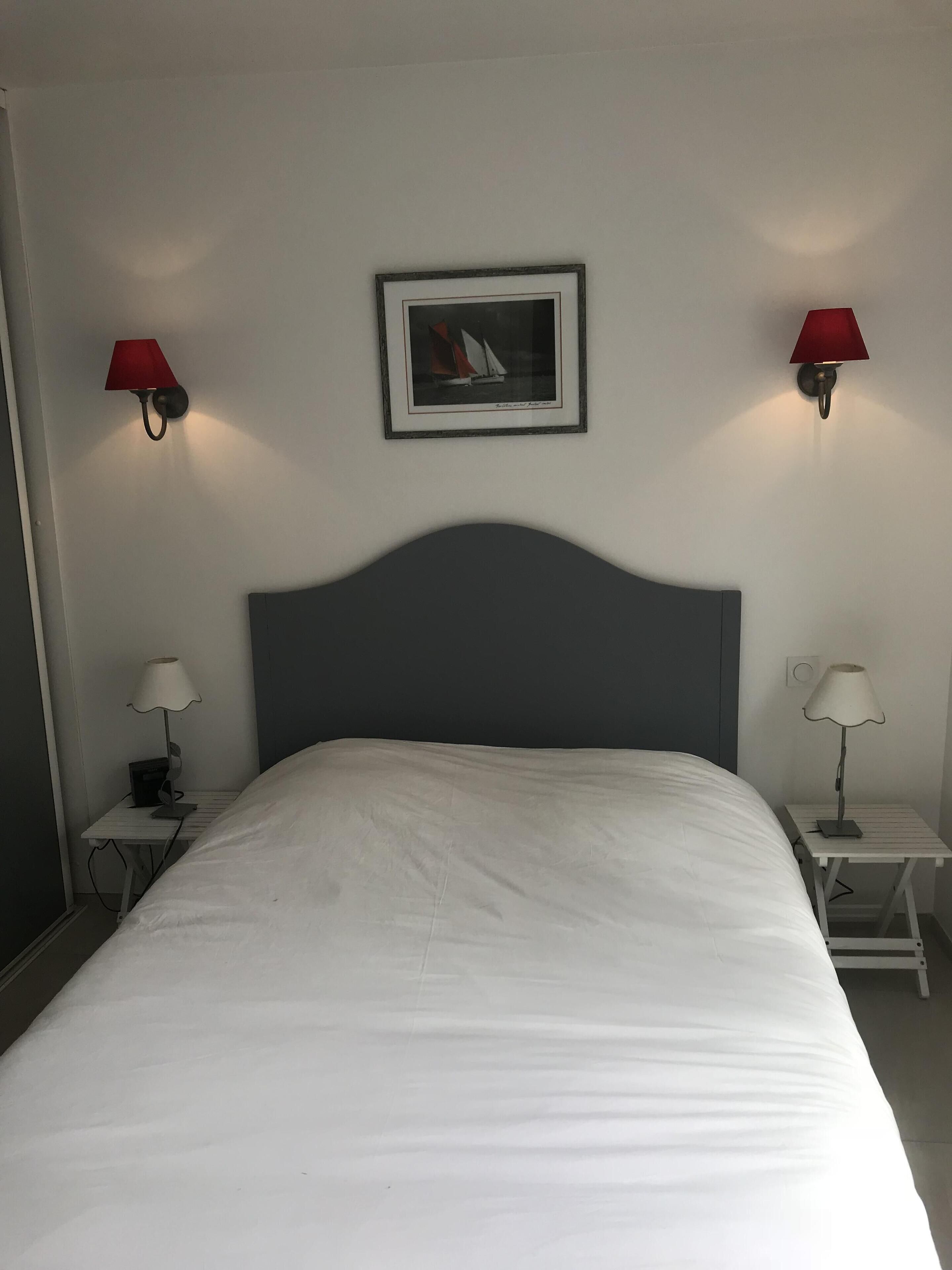 A neatly made bed in a hotel room with a dark headboard, two bedside tables with lamps, and a framed picture on the wall.