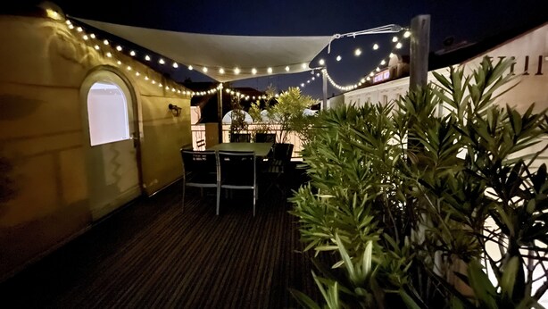 En udendørs patio med lyskæder, et bord, stole og plantekrukker.