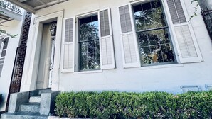 A two-story building with a balcony, large windows with shutters, and a brick-paved entrance.