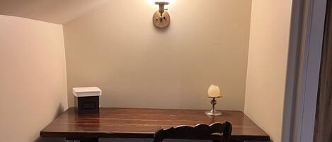 Un coin repas comprenant une table en bois, une chaise, un luminaire fixé au mur et une petite lampe de table.
