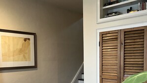A room with two upholstered chairs, a framed artwork on the wall, a staircase, and a wooden closet.