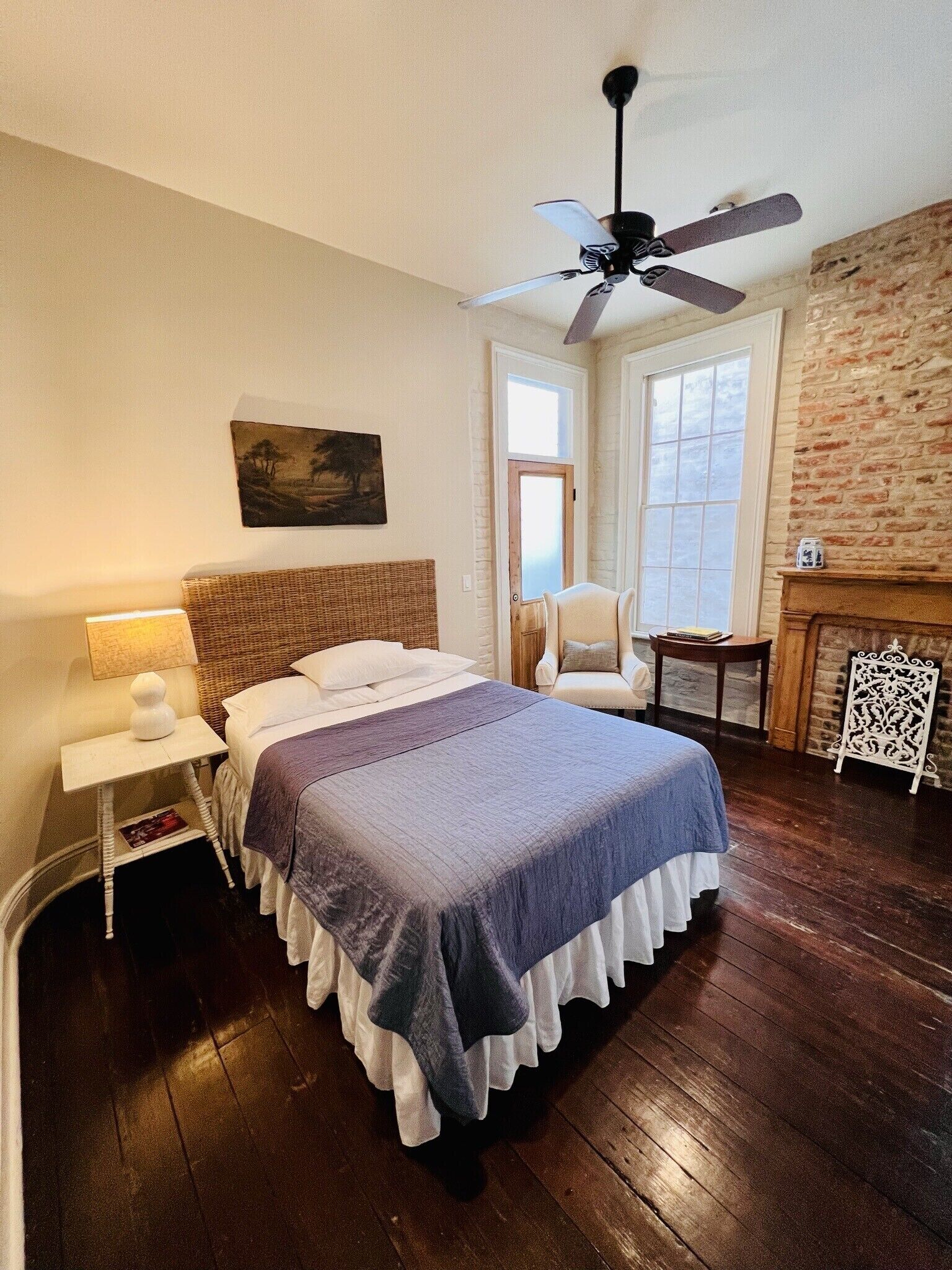 Un dormitorio con una cama grande, ventilador de techo, una silla, chimenea y ventana.
