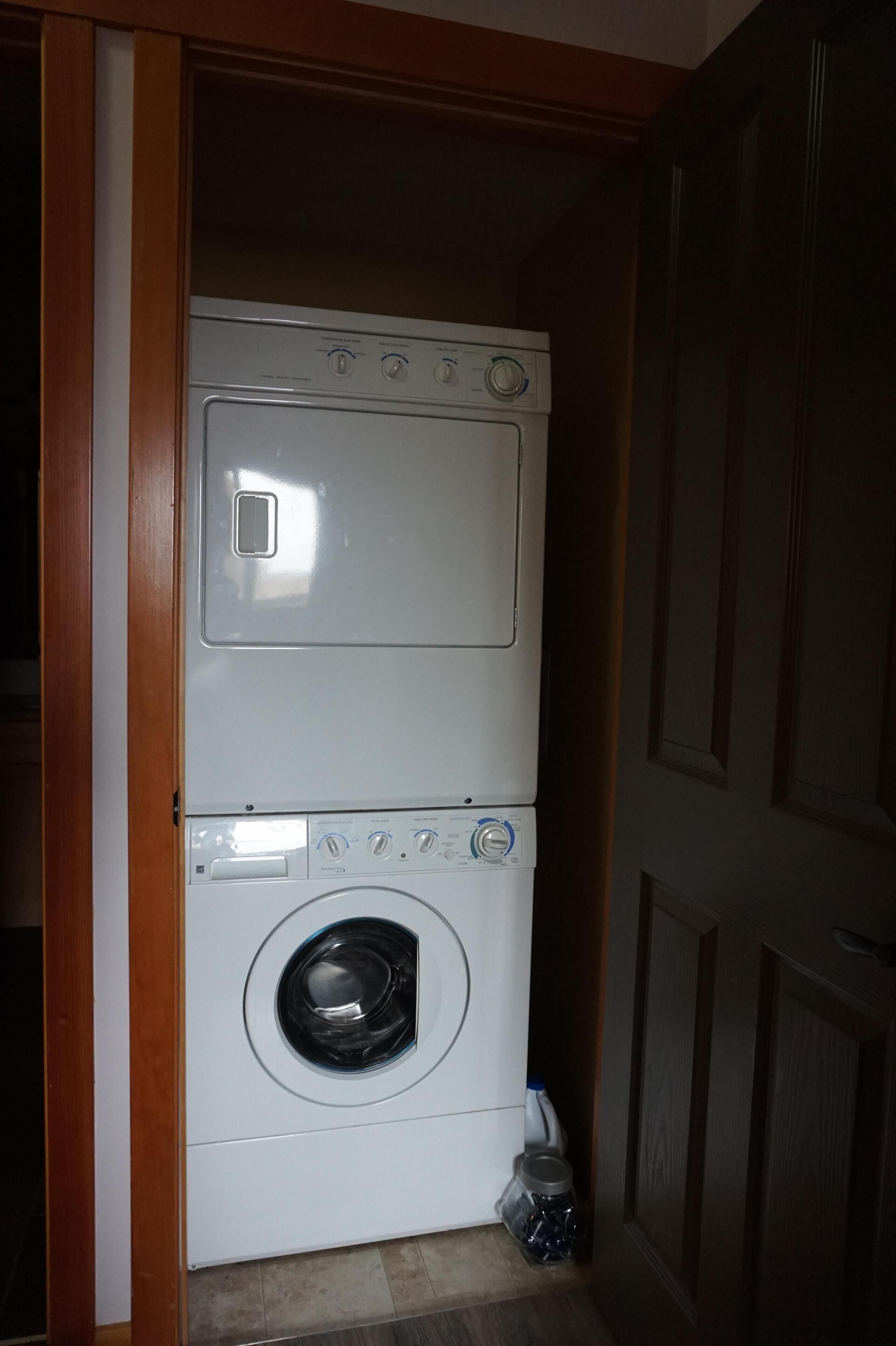 A front-loading washer and dryer unit in a laundry room with wooden doors and a tiled floor.