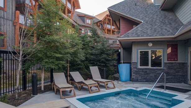 A pool area with lounge chairs and a hot tub, surrounded by buildings with wooden balconies. - Premium 2 Bedroom, 2 Bath Condo w/central Air Conditioning- Lodges at Canmore (Canmore)