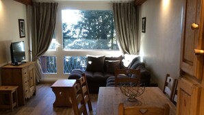 A cozy dining area with a wooden table and chairs, a sofa, and a television on a wooden cabinet.