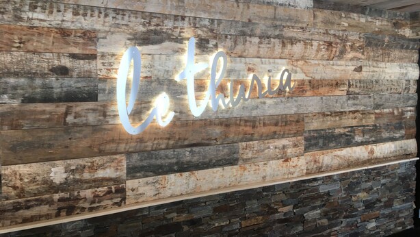 A rustic wall with a neon sign spelling "Lo thuria."