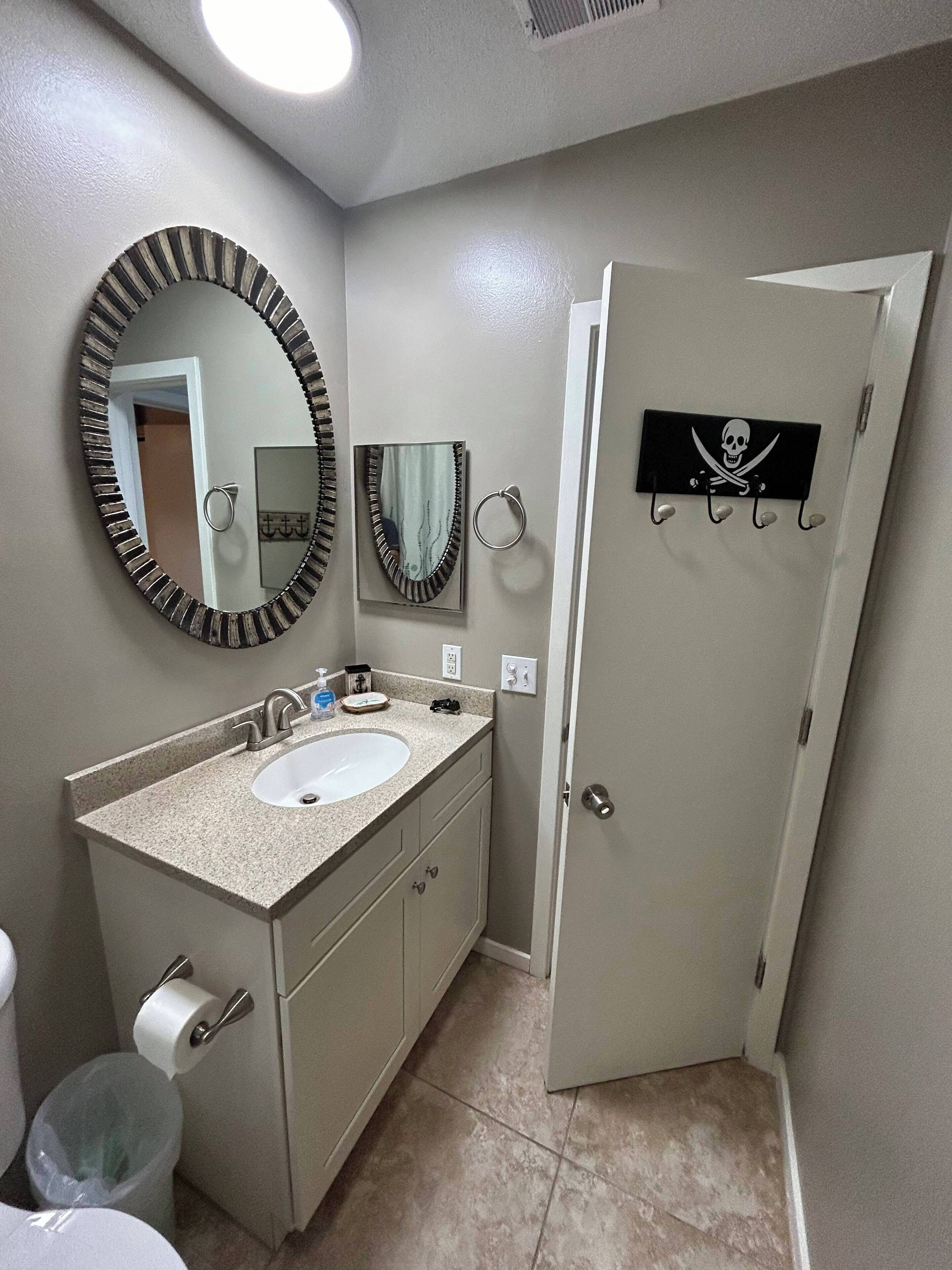 Un bagno con lavandino, specchio, water e una porta decorata con teschio e ossa incrociate.