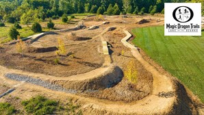 Vue aérienne d’un espace paysager avec des allées sinueuses et de jeunes arbres, entouré d’un champ herbeux et d’une forêt dense en arrière-plan.