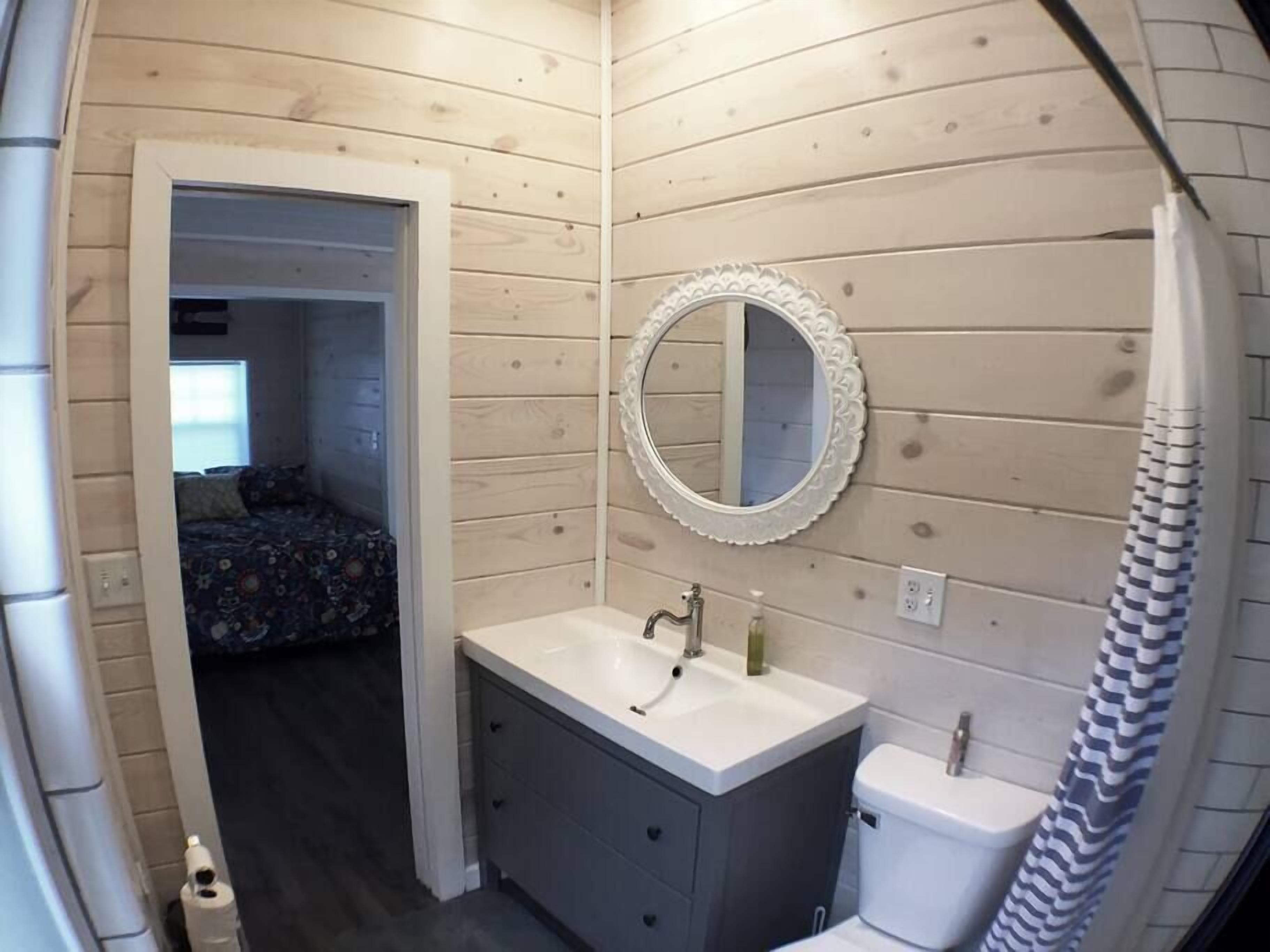 A compact bathroom with a wooden wall, a round mirror, a sink, and a toilet.
