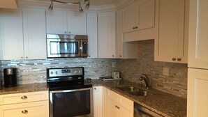 A modern kitchen with white cabinets, stainless steel appliances, a granite countertop, and a tiled backsplash.