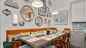 Un coin repas avec une table en bois dressée pour six personnes, entourée de chaises en bois. La pièce est agrémentée d’un mur blanc orné de divers miroirs encadrés et d’un grand tableau abstrait.