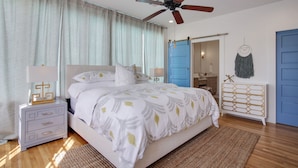 Une chambre à coucher comprenant un lit, une table de chevet, une commode et un ventilateur de plafond.