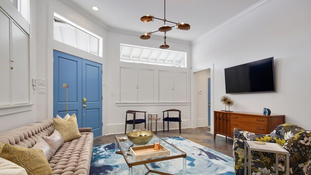 Un salon avec un canapé capitonné, une table basse en verre, un tapis bleu et un téléviseur à écran plat fixé au mur.