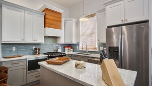 Une cuisine moderne avec des meubles blancs, un réfrigérateur en acier inoxydable et un îlot central en bois doté d’une planche à découper et d’un bloc à couteaux.