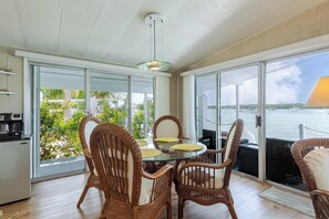 A dining area with wicker chairs, a glass table, and a view of the water.