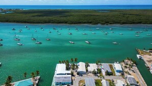 Une vue aérienne d’une marina où sont amarrés de nombreux bateaux, le tout entouré d’une végétation luxuriante et sous un ciel bleu clair.