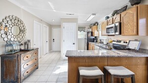 A kitchen with a granite countertop, wooden cabinets, a stainless steel refrigerator, and a microwave. There are two stools at the island. - Next to Silver Dollar City, King Master, 2BR 2BA, Full Size Kitchen, 20ft Patio (Branson)