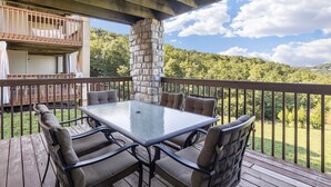 A covered outdoor deck with a glass-top table and six chairs, overlooking a lush green landscape. - Next to Silver Dollar City, King Master, 2BR 2BA, Full Size Kitchen, 20ft Patio (Branson)