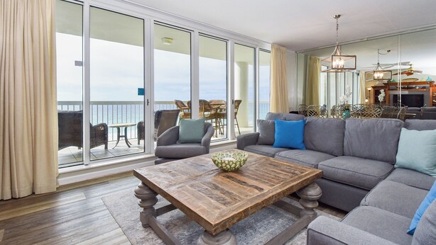 A spacious living room with a large gray sofa, a wooden coffee table, and a view of the ocean through large sliding glass doors. - Beachfront elegance w/3 beds, 3 baths, & private balcony! (Destin)