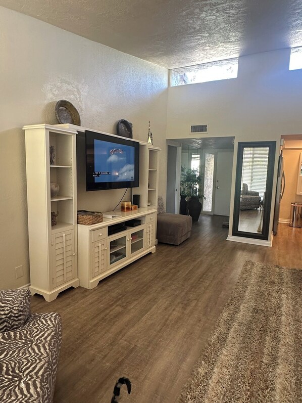 Sala de estar con televisor, mueble blanco de entretenimiento y vista al comedor.