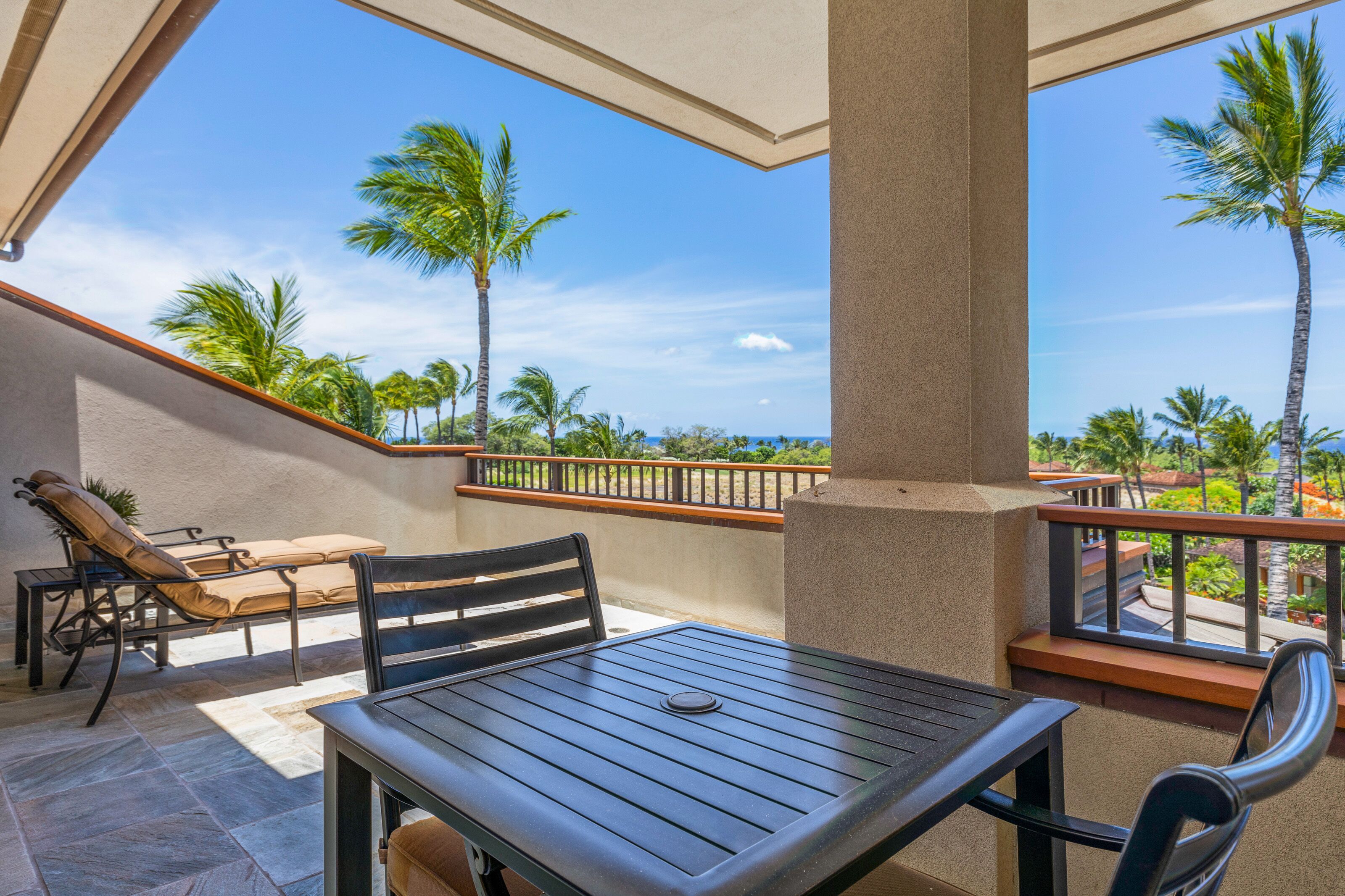 A balcony with a table and chairs, overlooking palm trees and a clear sky.