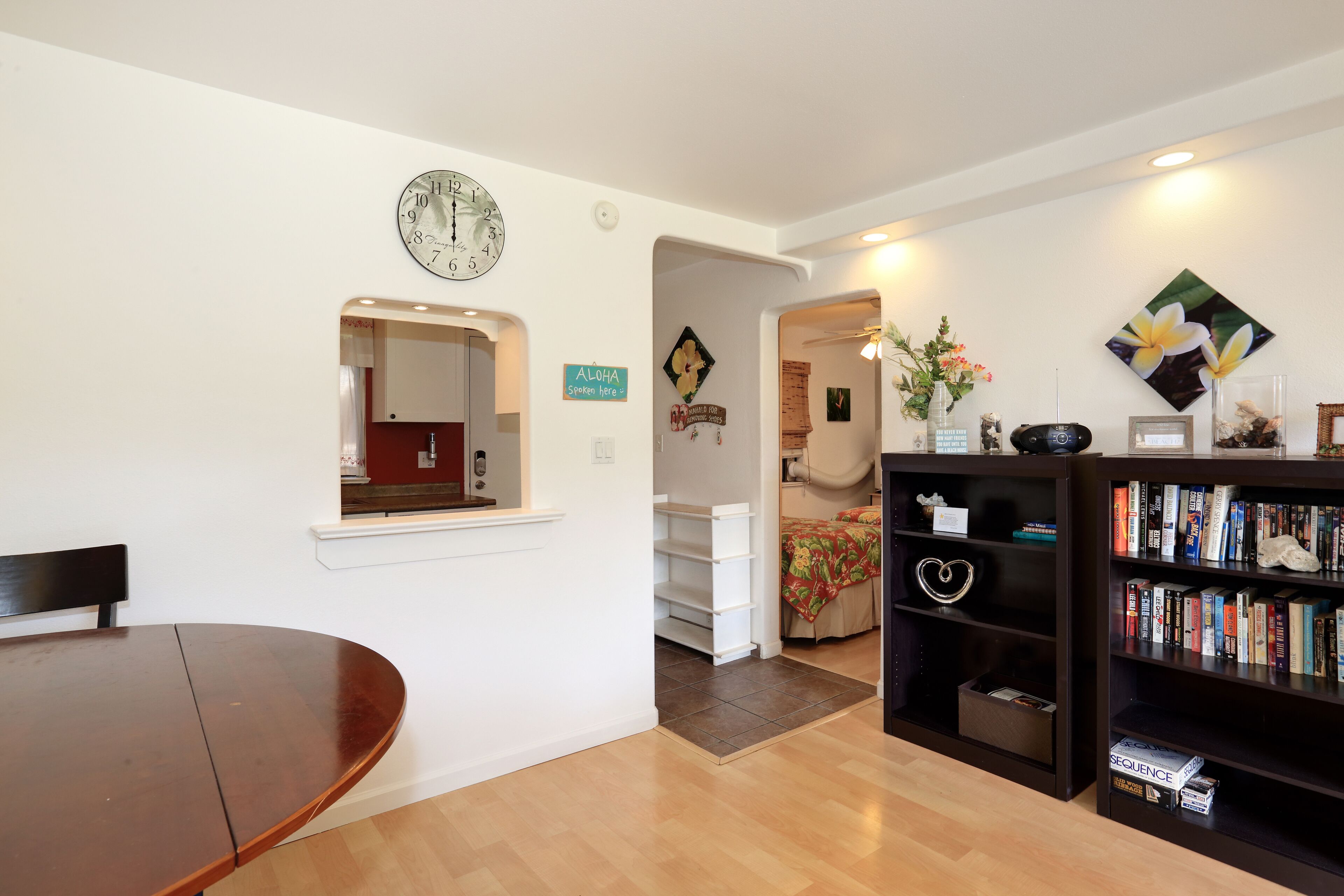 Un salon avec une table à manger en bois, une bibliothèque, une horloge et une petite plante décorative.