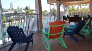 A covered outdoor area with chairs and a table, overlooking a swimming pool and palm trees. - Oceanside, pet friendly, 5/3 smart home with paddle equip.-SUPs, kayaks & canoe (SugarLoaf)