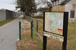 A pedestrian and bicycle path sign, a map of Cape Henlopen State Park, and a sign indicating the Junction and Breakwater Trail is 5.1 miles away.