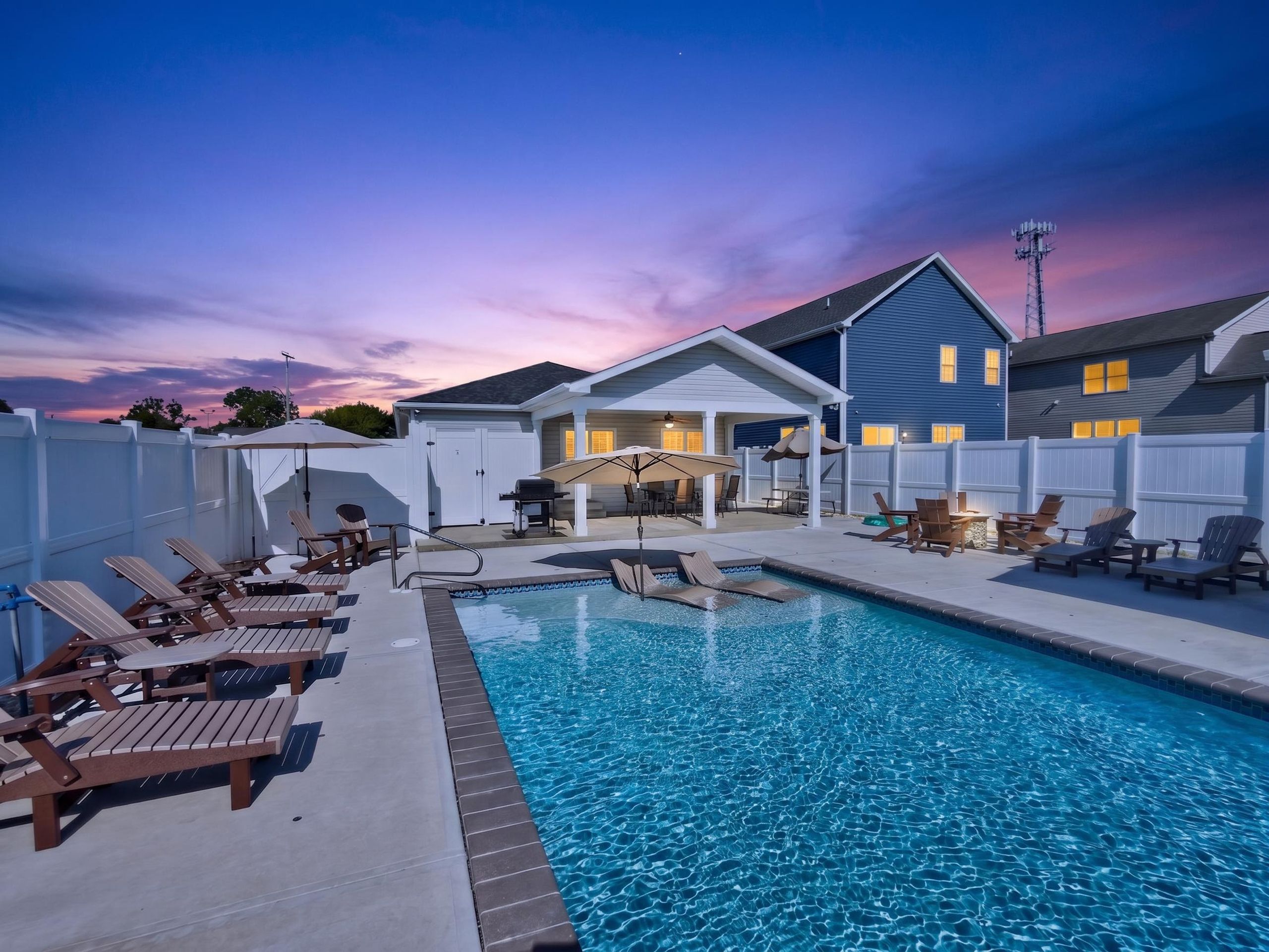 A backyard with a swimming pool, lounge chairs, a barbecue area, and a covered patio.