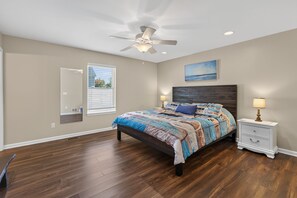 Quarto com cama, ventilador de teto, janela, mesa de cabeceira e um quadro na parede.