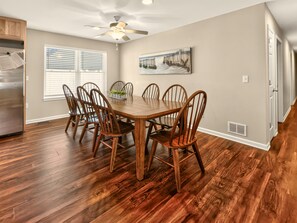 Uma área de refeições com mesa e cadeiras de madeira, um ventilador de teto e um quadro na parede.