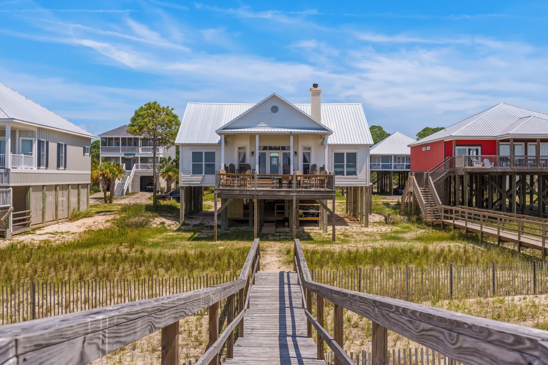A beachfront property with a wooden walkway leading to a house with a balcony.