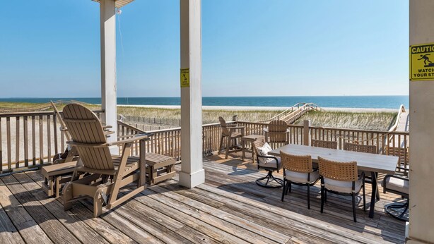 Une terrasse en bois, agrémentée de chaises et de tables, qui offre une vue sur la plage.
