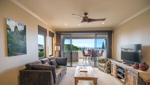 A spacious living room with a sofa, coffee table, and TV. There is a balcony with a view of greenery. - Kapalua Golf Villa 20T5 Relax & Unwind (Kapalua)
