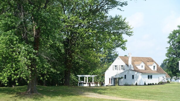 Une maison blanche avec un porche et un grand arbre devant.