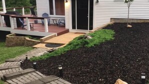 Un jardin aménagé à l’arrière de la maison, avec une terrasse, des marches et un petit arbre.