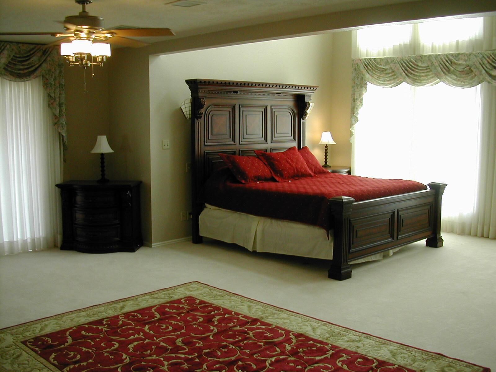 A bedroom with a large bed, a nightstand, a dresser, a ceiling fan, and a window with curtains.