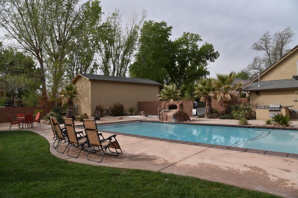 A backyard with a swimming pool, a patio with chairs, and a small waterfall feature. - Luxury Home and Property with 2 Private Pools and Pickleball Court (Saint George)