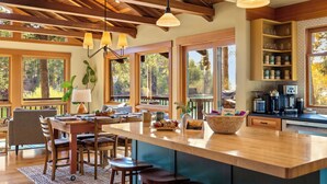 Une cuisine spacieuse dotée d’un grand îlot central, de poutres apparentes en bois au plafond et de grandes fenêtres offrant une vue sur l’extérieur.