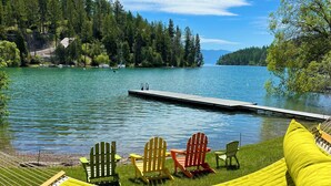 Une vue sur le lac avec un quai, des fauteuils Adirondack verts et rouges, un hamac jaune et une zone herbeuse.