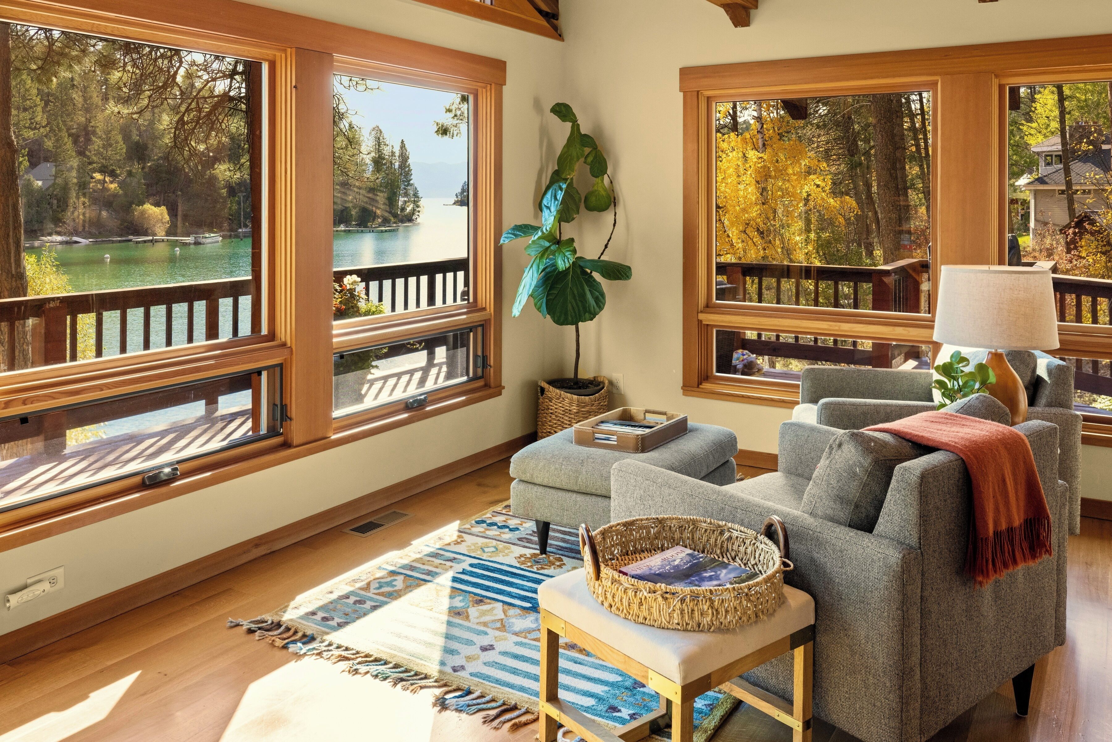 Una sala de estar acogedora con ventanas amplias, un sofá confortable, una mesita y vistas a un lago y un bosque.