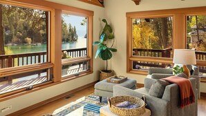 Un salon chaleureux avec de grandes fenêtres, un canapé confortable, une petite table et une vue sur un lac et une forêt.