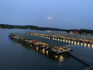 A marina with multiple docked boats and covered structures, surrounded by water and hills in the background.